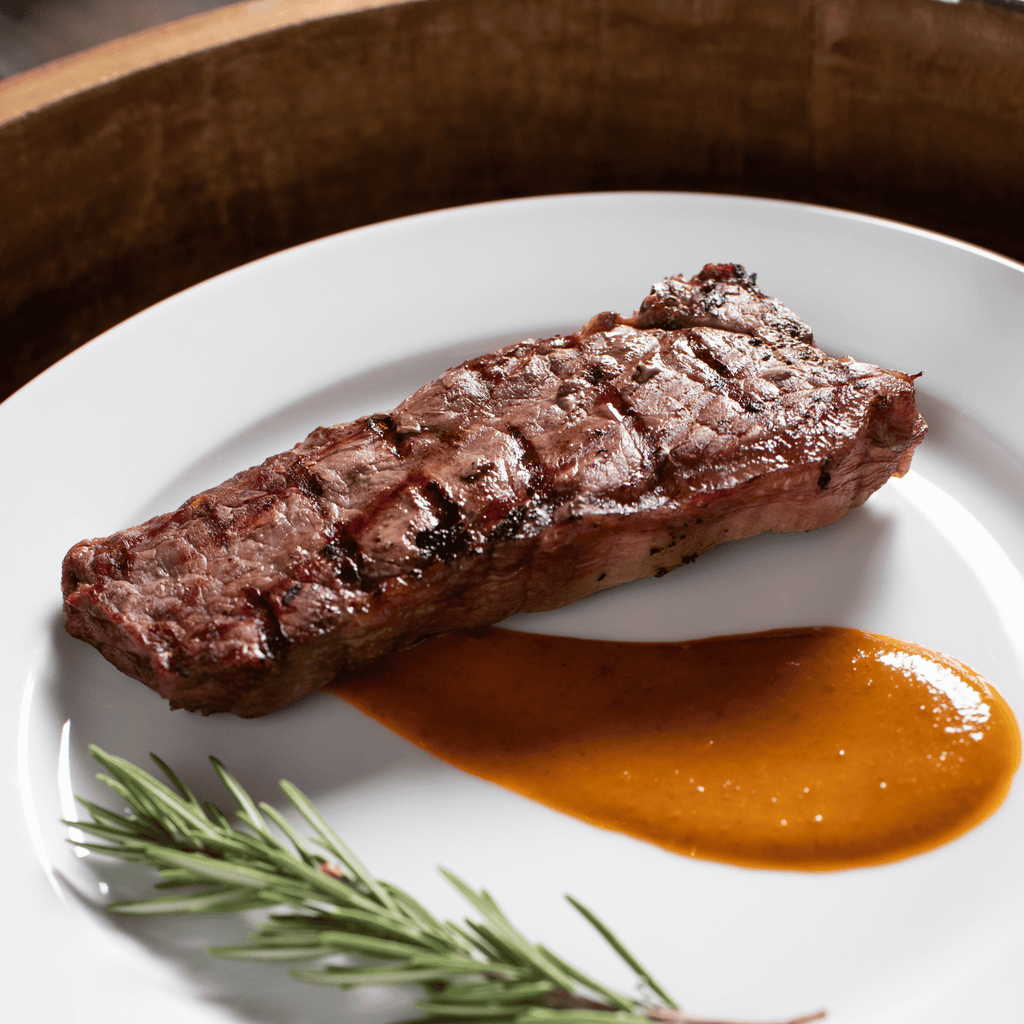 Grilled bison NY strip steak on a white plate with a side of sauce and rosemary.