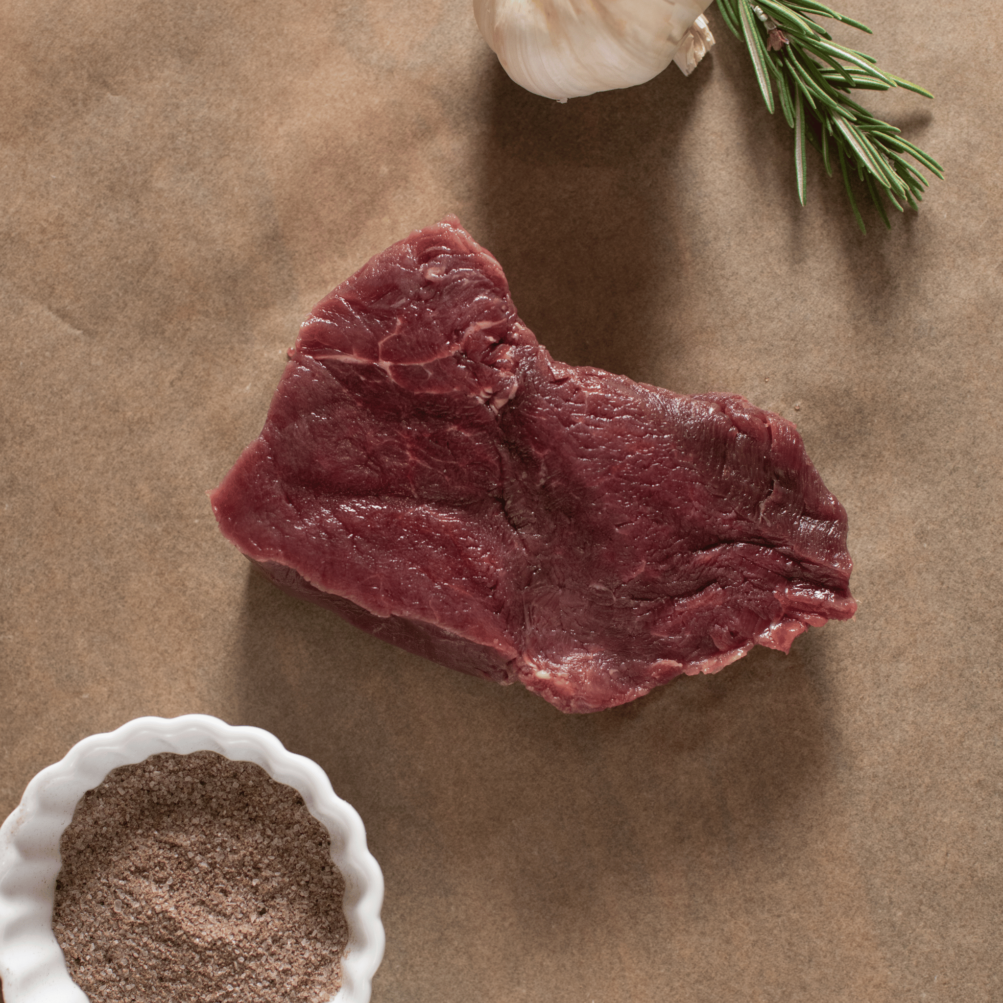 Raw bison filet steak with herbs and spices on a brown surface
