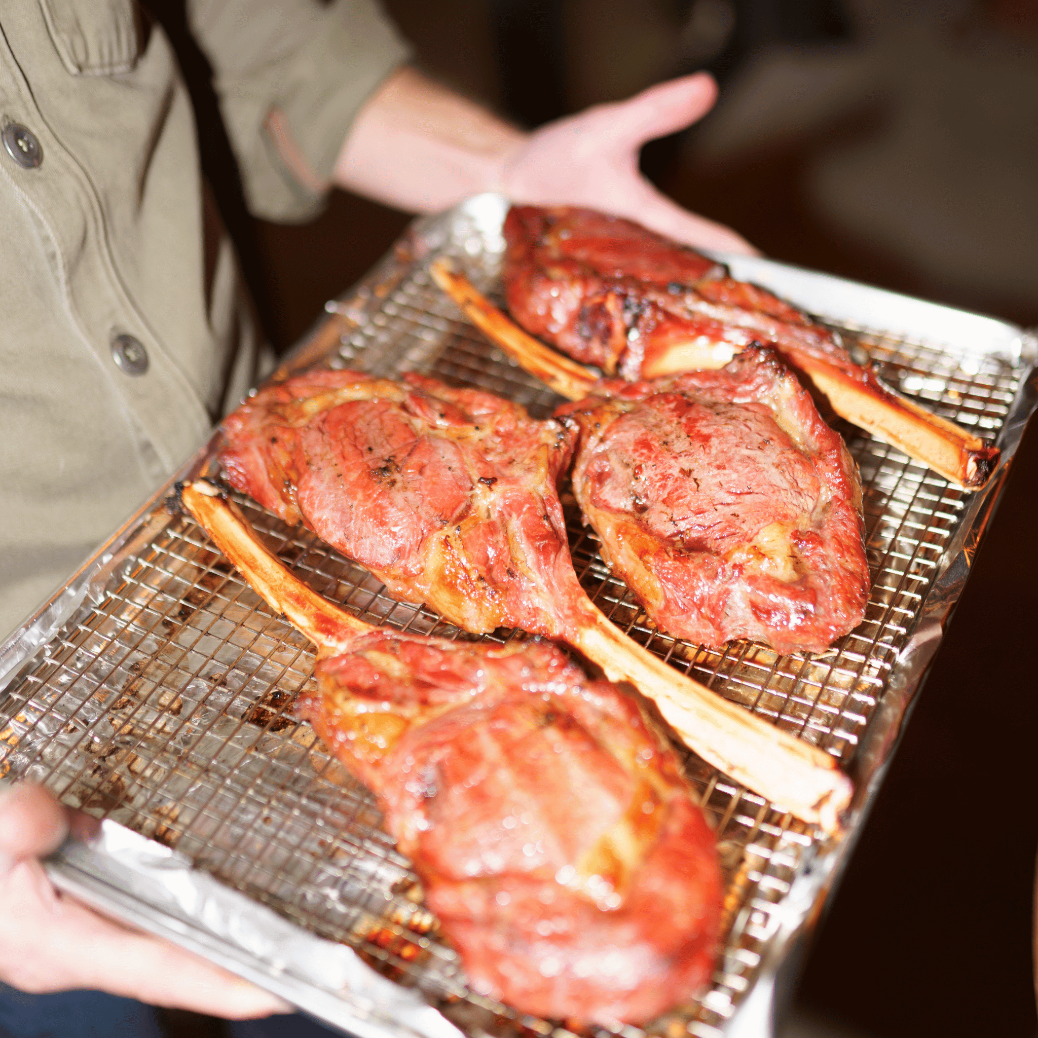 Person holding a tray with reverse seared bison tomahawk steaks.