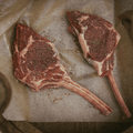 Two raw seasoned bison tomahawk steaks on a piece of parchment paper.