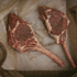 Two raw seasoned bison tomahawk steaks on a piece of parchment paper.