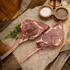 Two raw bison tomahawk steaks on a wooden surface with salt and pepper.