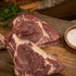 Two pieces of raw bison steaks on a wooden cutting board with a small bowl of salt.
