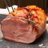 Roasted ham being sliced with a knife on a dark surface