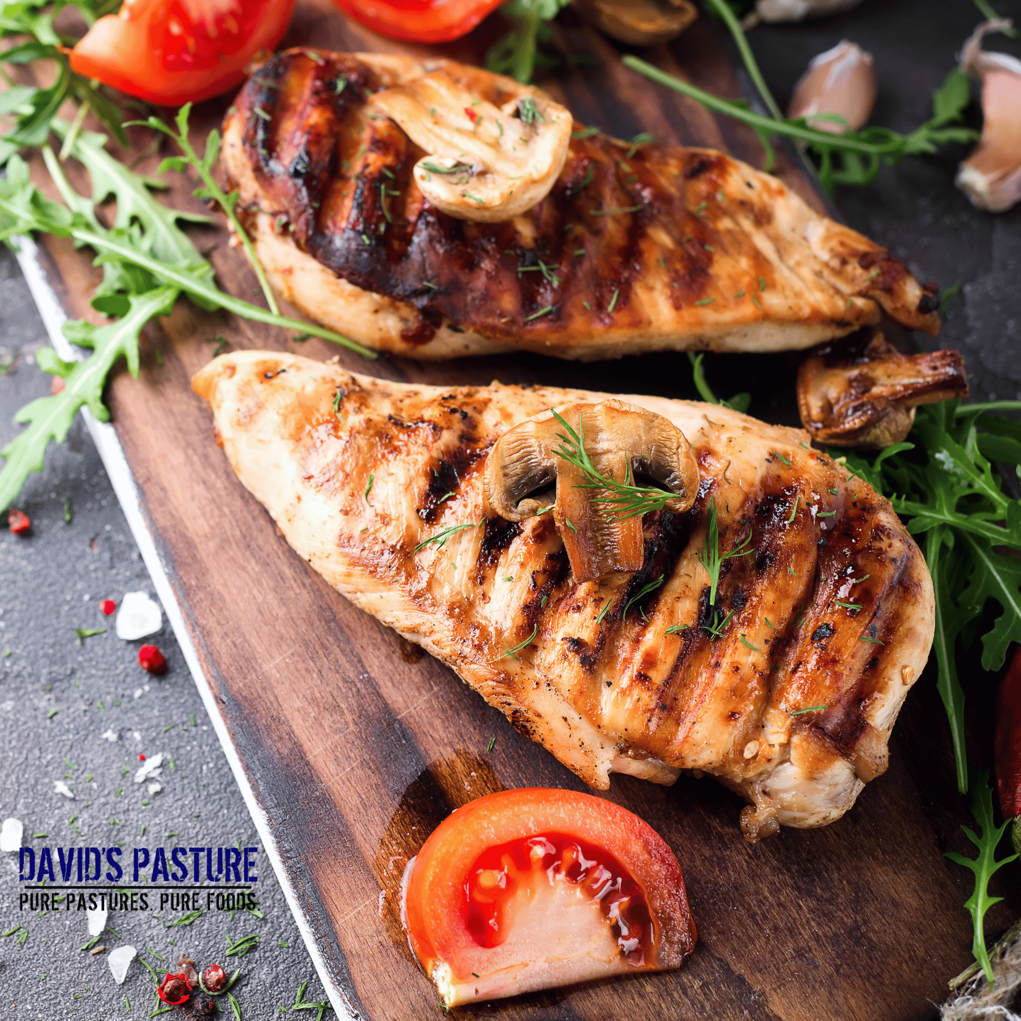 Grilled chicken breast on a wooden cutting board with tomatoes and herbs, featuring 'David's Pasture' branding.