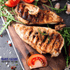 Grilled chicken breast on a wooden cutting board with tomatoes and herbs, featuring 'David's Pasture' branding.