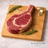 Raw steak on a wooden cutting board with rosemary and garlic, Plainview Beef Co. branding visible.