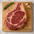 Raw ribeye steak on a wooden cutting board with herbs and spices, Plainview Beef Co. branding visible.