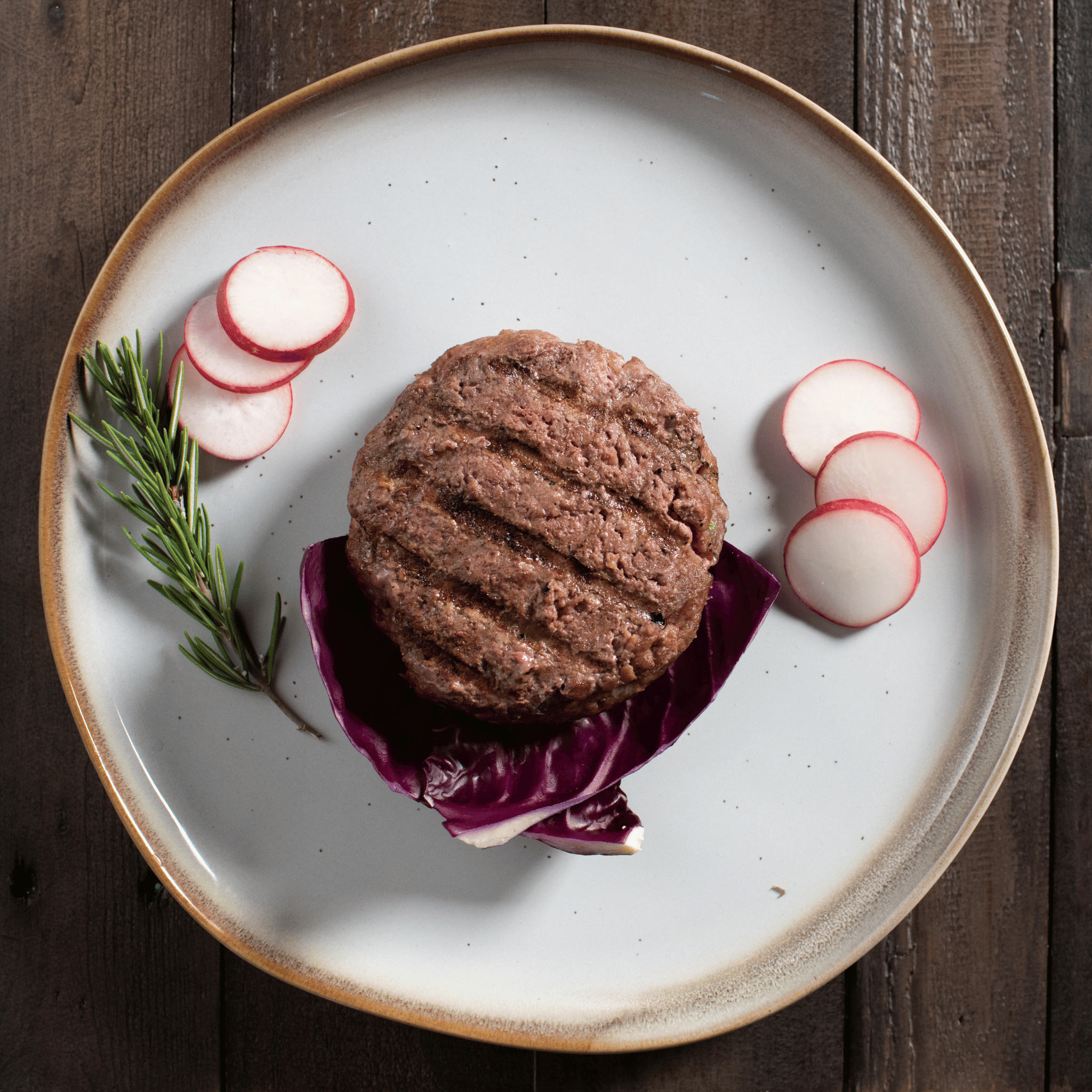 Grilled bison burger on a plate with radishes and purple cabbage on a wooden surface