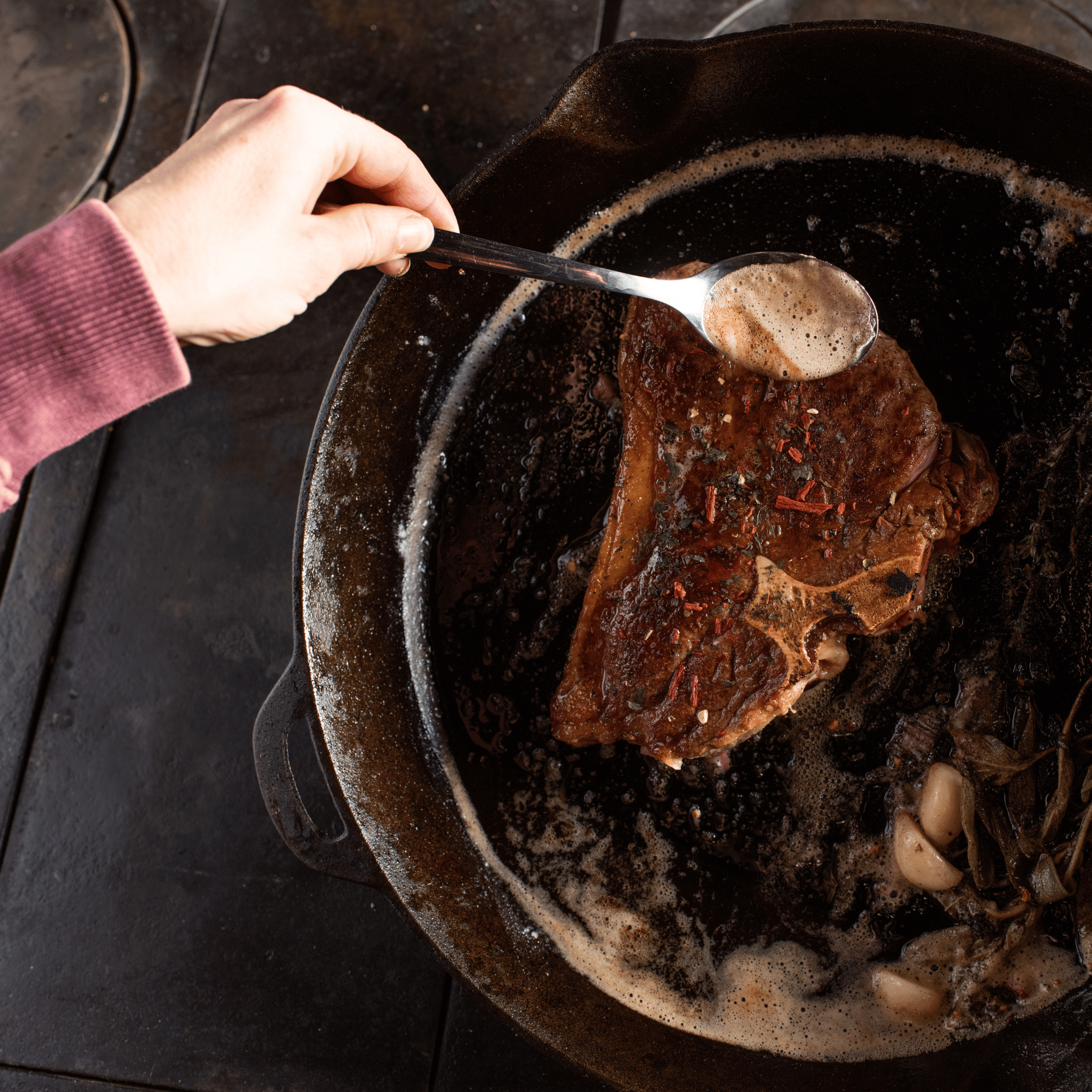 Person spooning sauce over a bison steak in a cast iron skillet