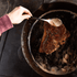 Person spooning sauce over a bison steak in a cast iron skillet