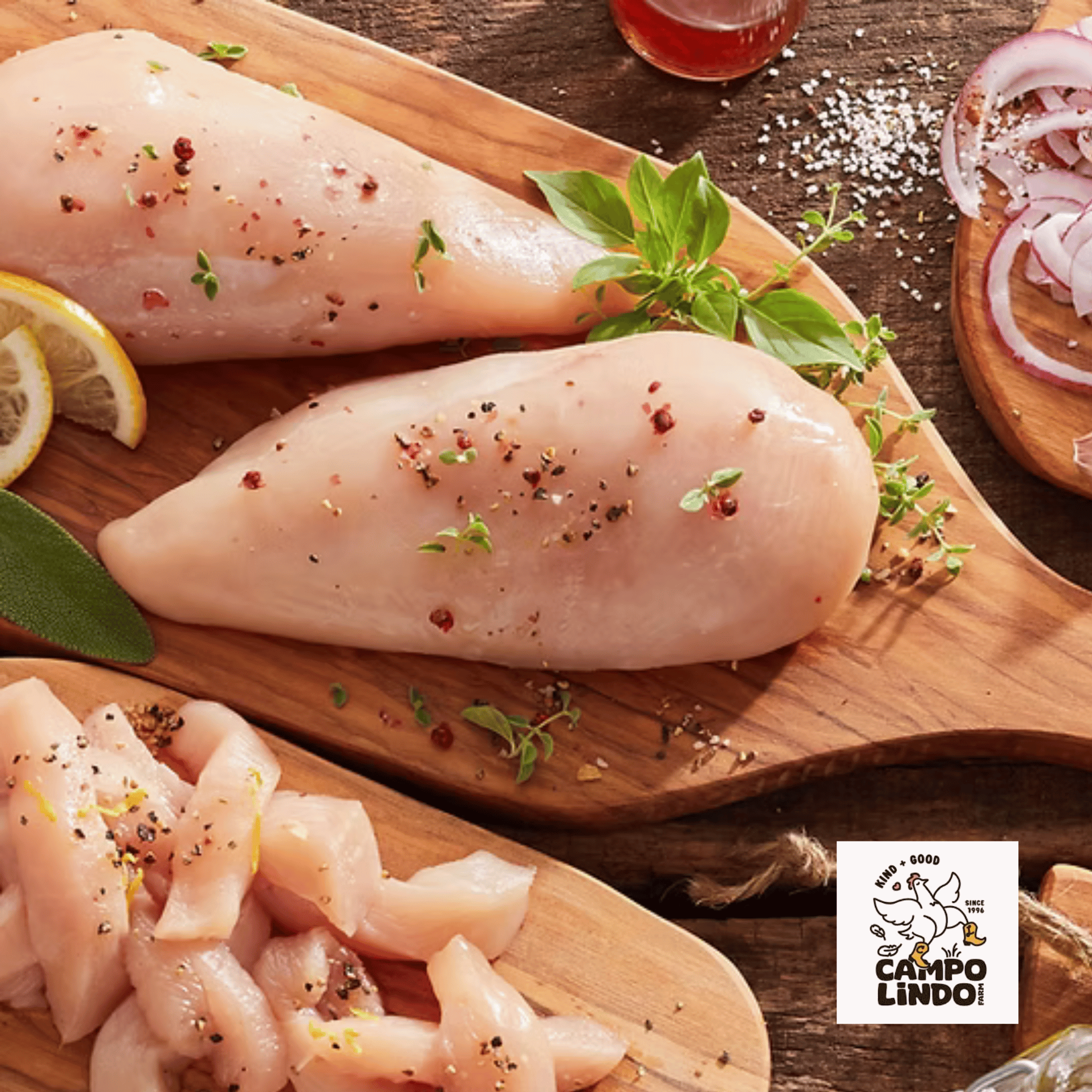 Raw chicken breasts on a wooden board with herbs and spices, Campo Lindo logo visible.