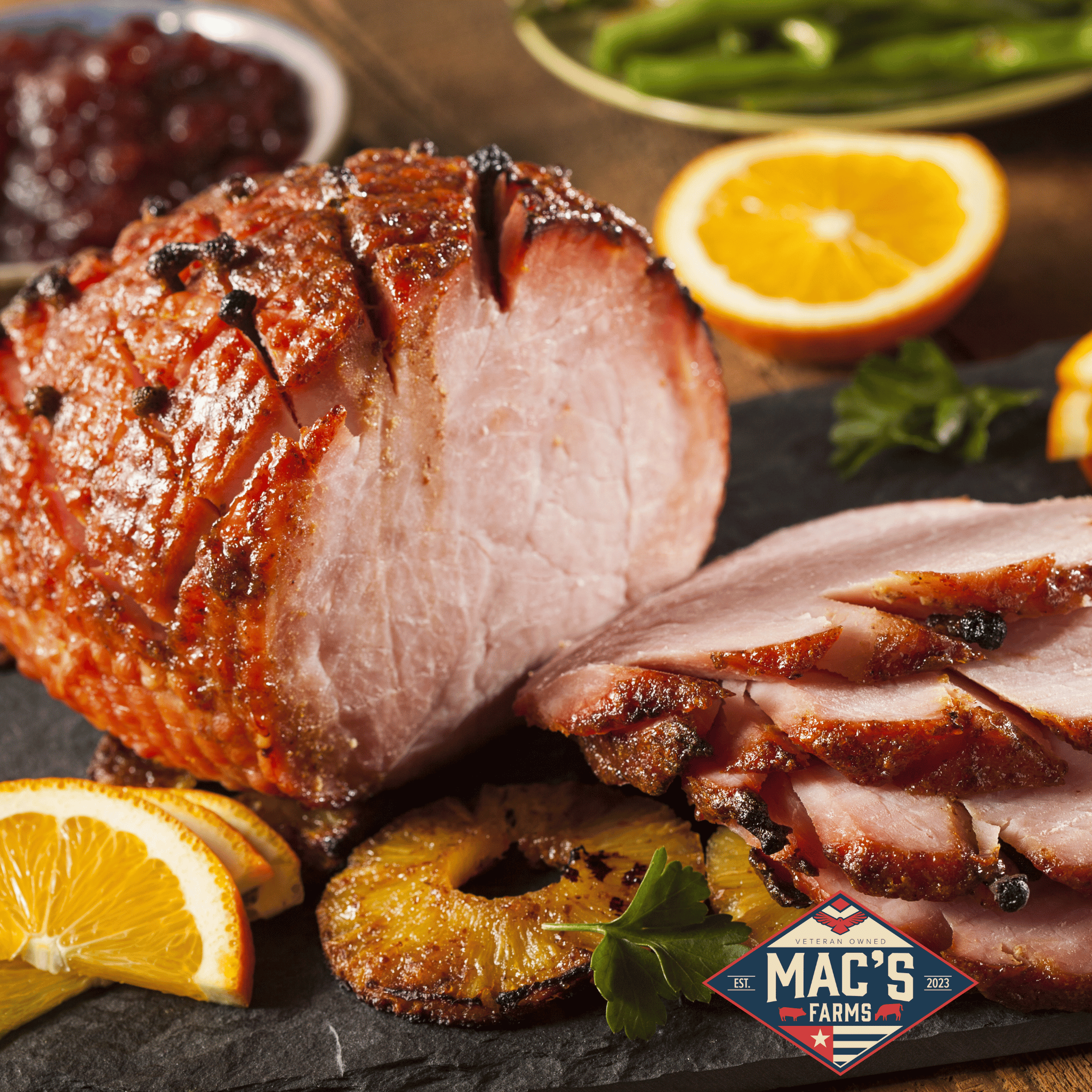 Sliced roasted ham with oranges and pineapple on a slate board, featuring Mac's Farms logo.